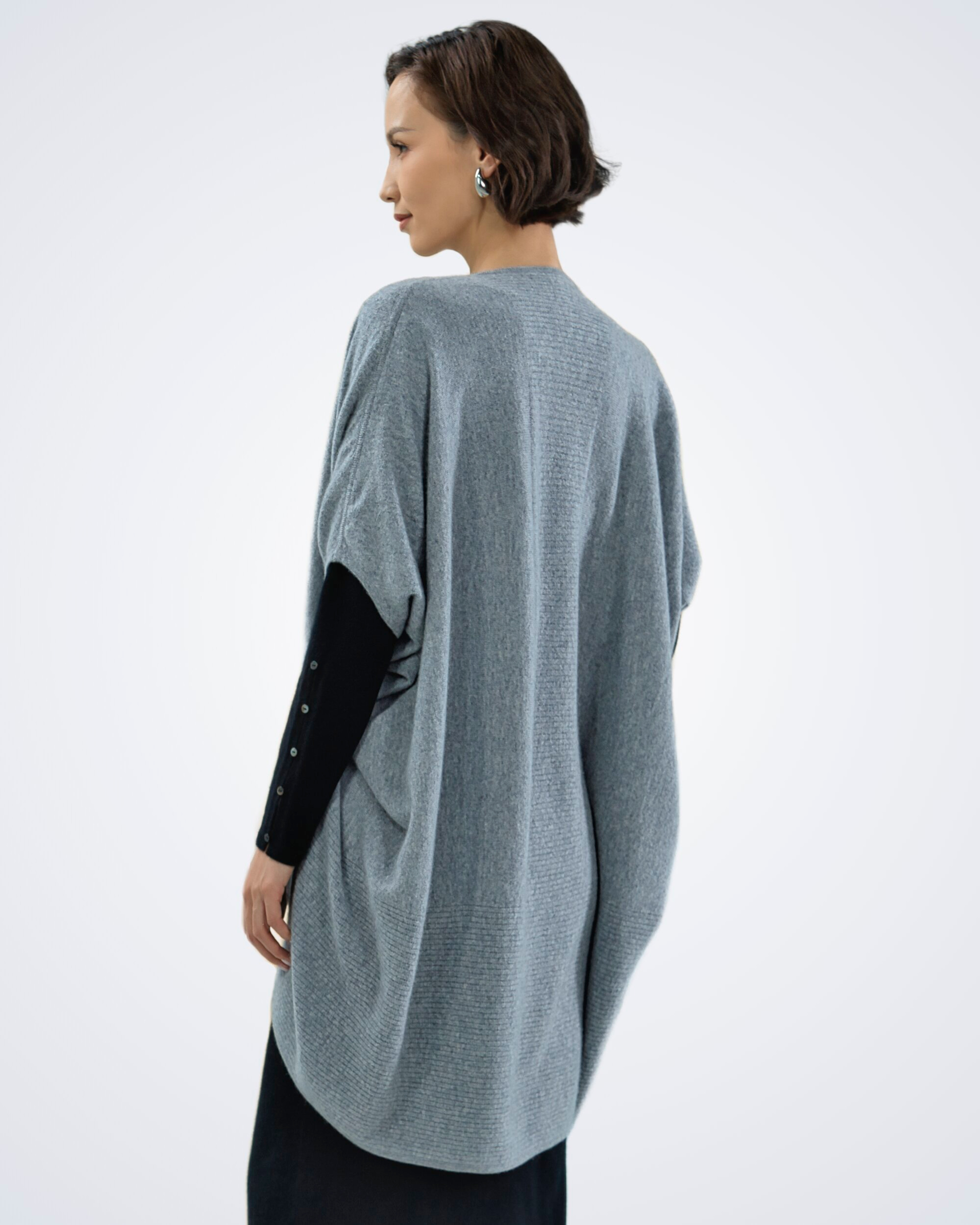 Unur model wearing a light grey open-front cashmere poncho with ruched sleeves, back view