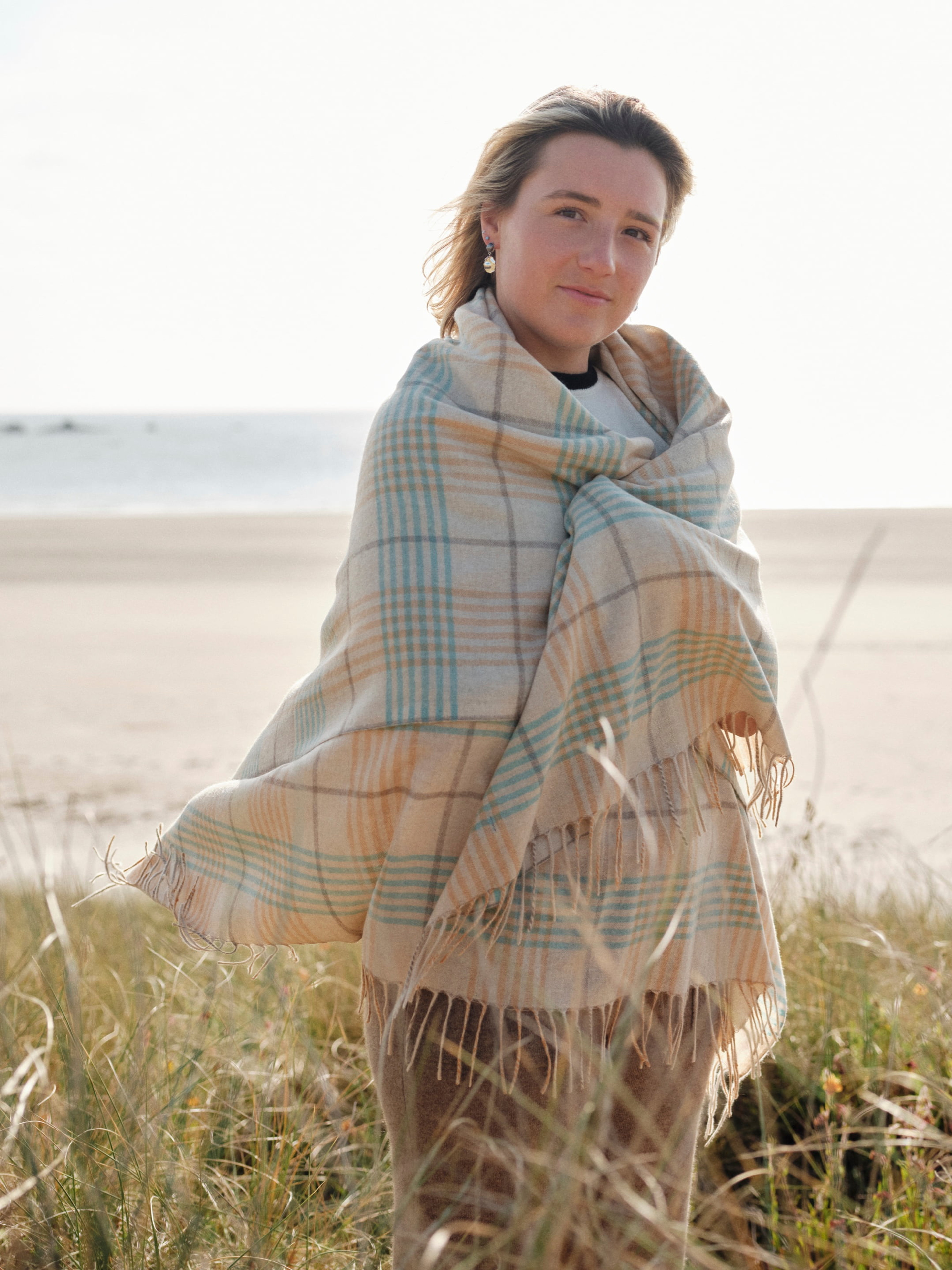 Model outdoors wearing a cashmere plaid wrap shawl with tasselled edges