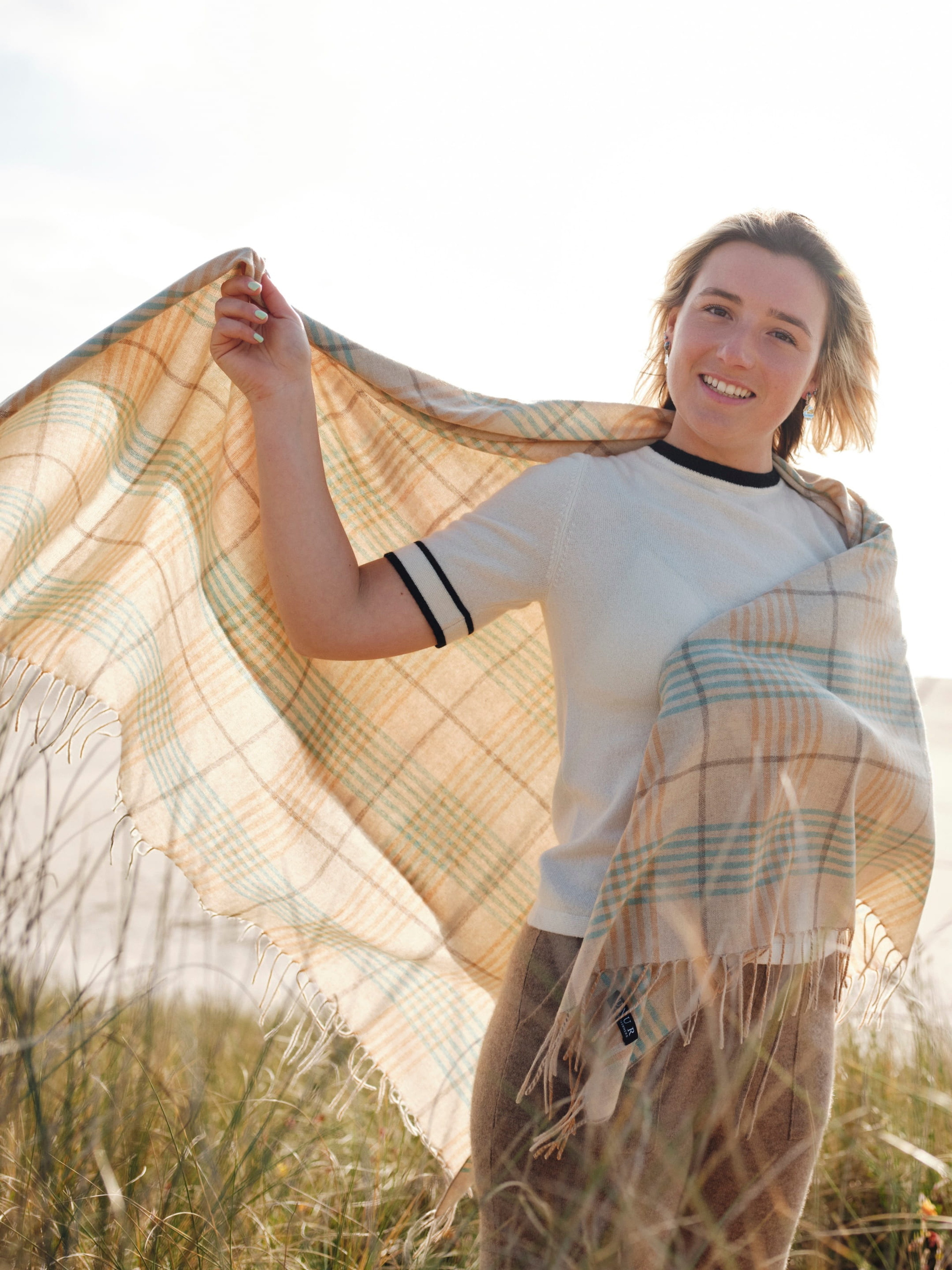 Model outdoors wearing a cashmere plaid wrap shawl with tasselled edges