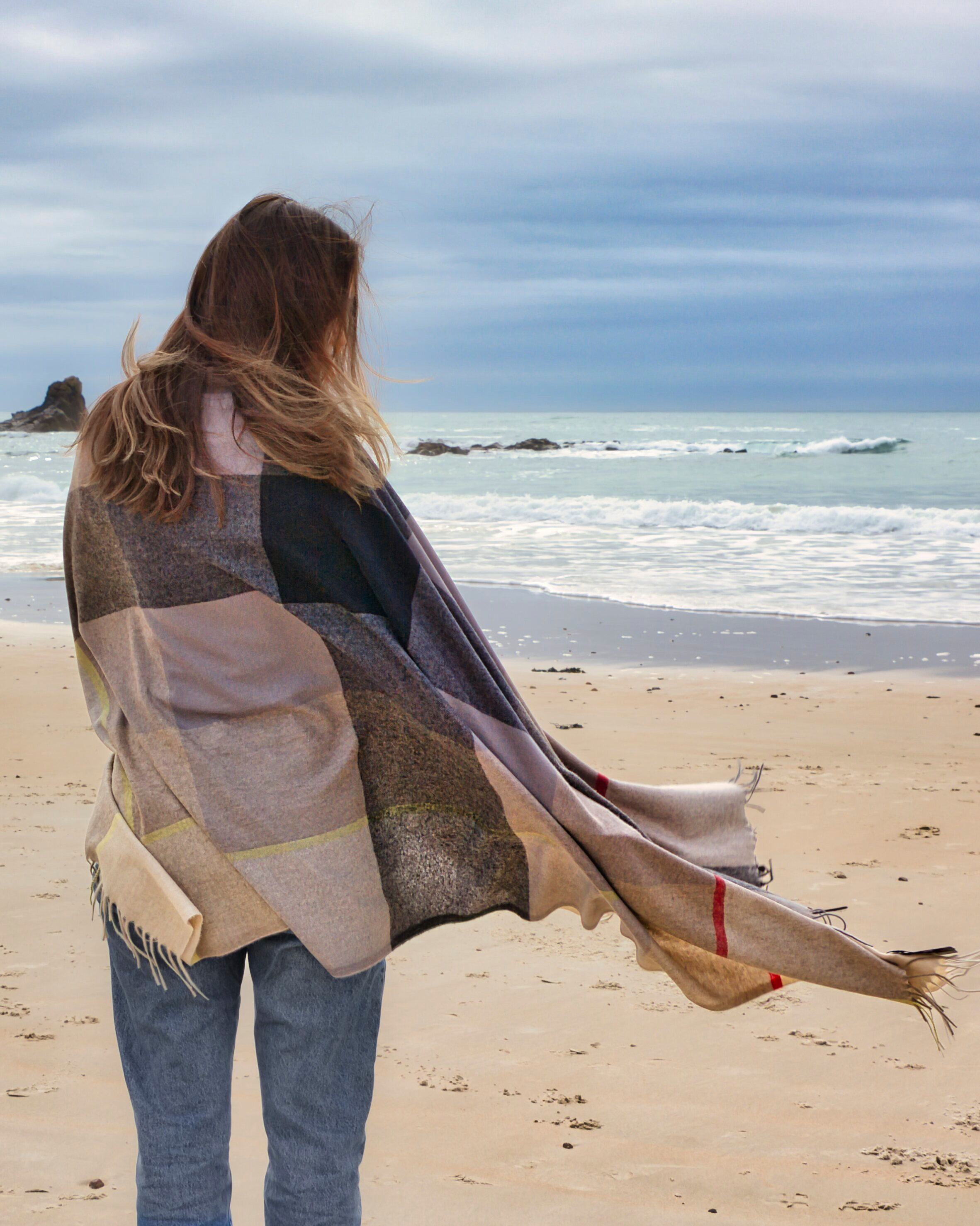 Woman on the beach wrapped in a check plaid cashmere wrap shawl
