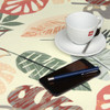 Wipe Clean Tablecloth - Navarra: Monstera.  Pictured with a cup and sauce, 'phone, and pen.