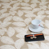 Wipe clean tablecloth. Living Feathers - Beige. Pictured with a cup and saucer, 'phone, pen and coins.