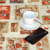 Navarra Love Christmas Wipe Clean Tablecloth. Pictured on a table with a phone, cup and pen