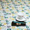 Living Cassatt Wipe Clean Tablecloth. Pictured with a cup and saucer, 'phone, pen and coins.