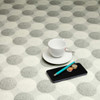 Living Circles Grey: Wipe Clean Tablecloth. Pictured with a cup and saucer, 'phone, pen and coins.