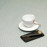 Acrylic Coated Tablecloth. Living Dottie - Ash Grey. Pictured with cup and saucer, 'phone, and pen.