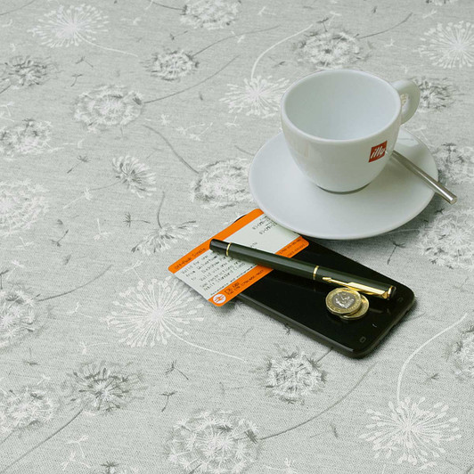 Living Glam Dandelion wipe clean acrylic coated tablecloth. Pictured with a cup,saucer, 'phone and pen.