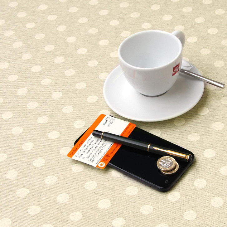 Acrylic Coated Tablecloth - Mirha Polka Beige shown on a table with a cup ,saucer.phone and pen.