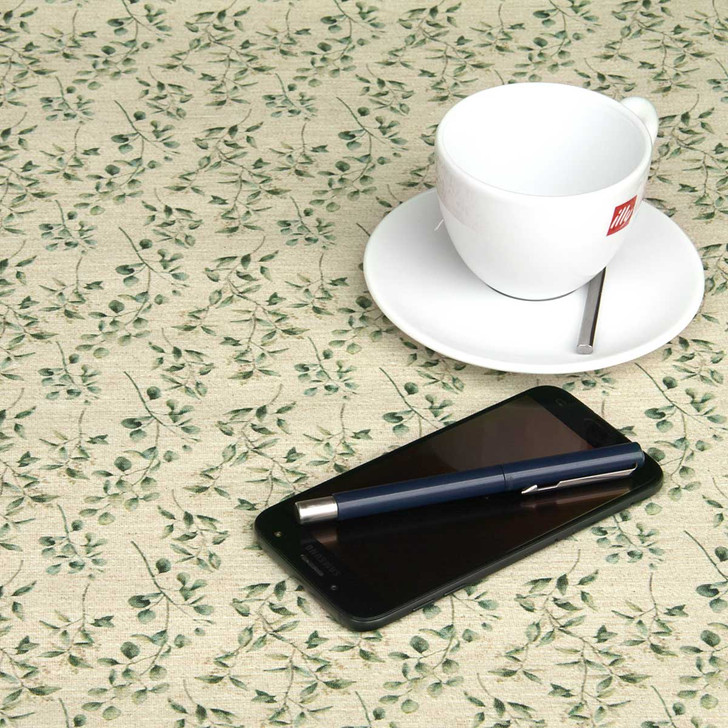 Wipe Clean Tablecloth - Culla: Vert. Shown on a table with a cup, saucer, pen and phone