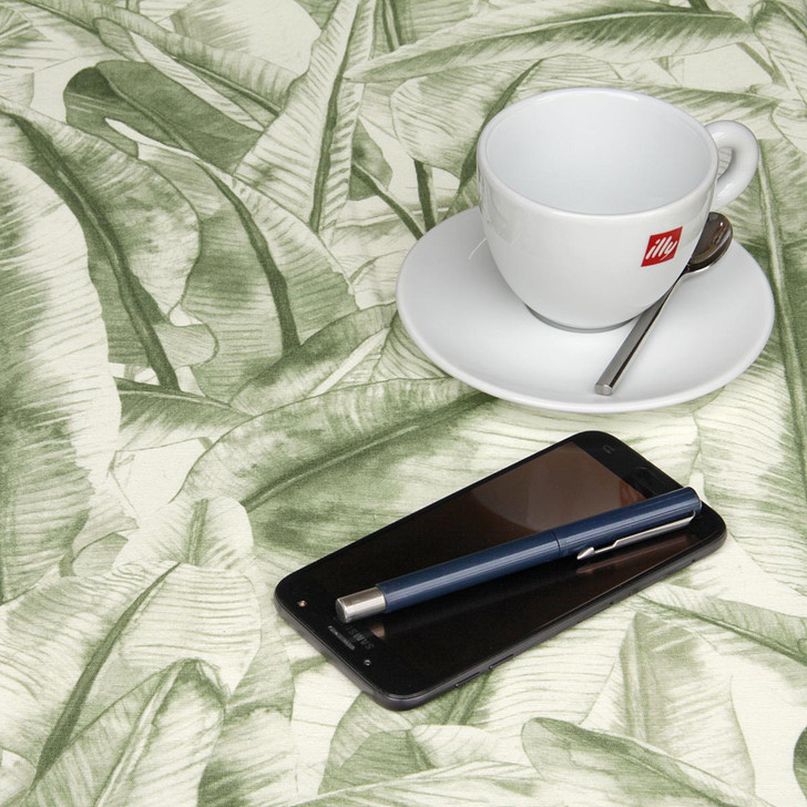 Wipe Clean Tablecloth - Navarra: Leaves - Green. Pictured with a cup and saucer, 'phone and pen.