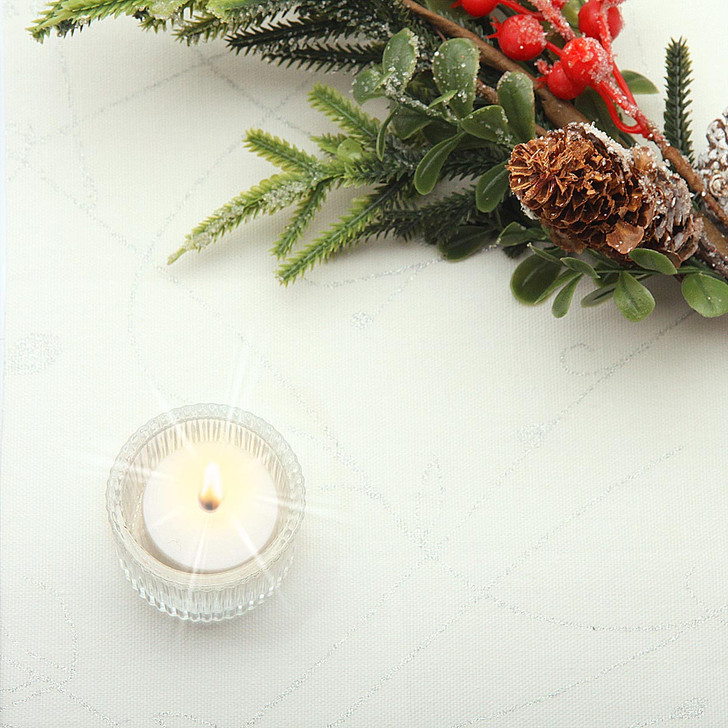 Wipe Clean Tablecloth - Blaze: Silver Sprig. Pictured on a table with a votive tealight candle and seasonal greenery.