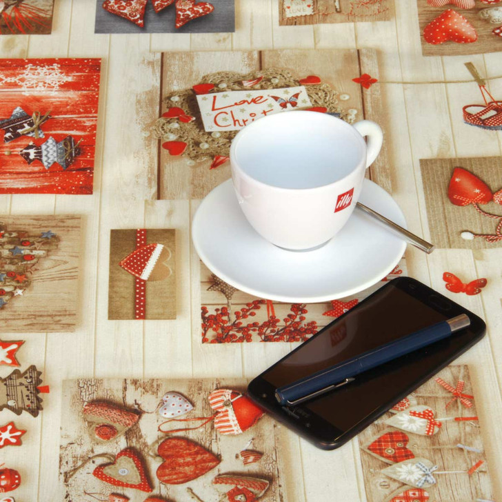 Navarra Love Christmas Wipe Clean Tablecloth. Pictured on a table with a phone, cup and pen
