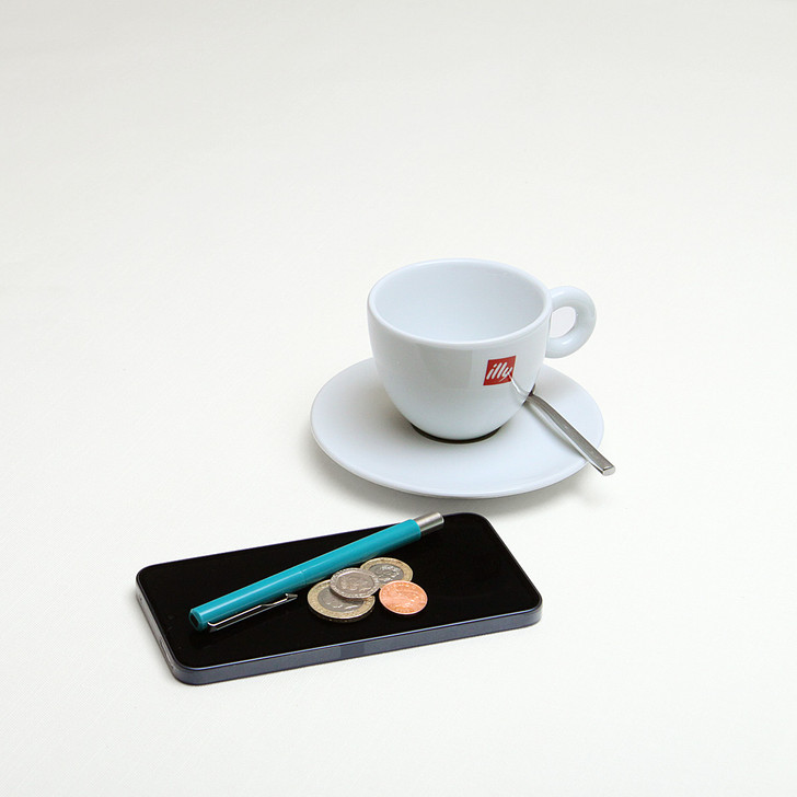Wipe Clean Tablecloth - Blaze: White. Pictured with a cup and saucer, 'phone, pen and coins.