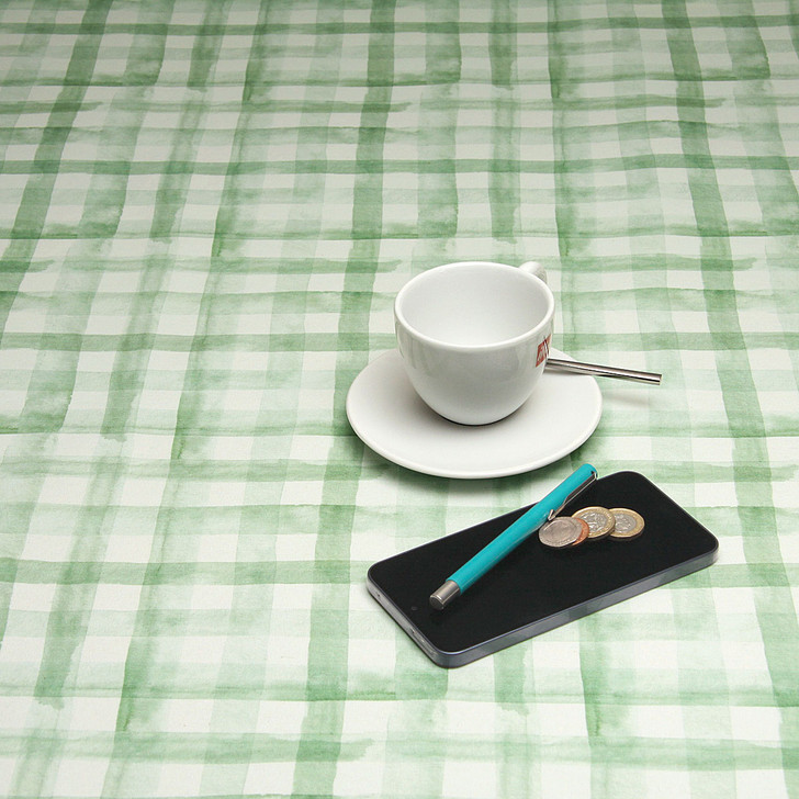 Navarra: Green Plaid.  Acrylic Coated Tablecloth, pictured on a table with a cup and saucer,  'phone, pen and coins.