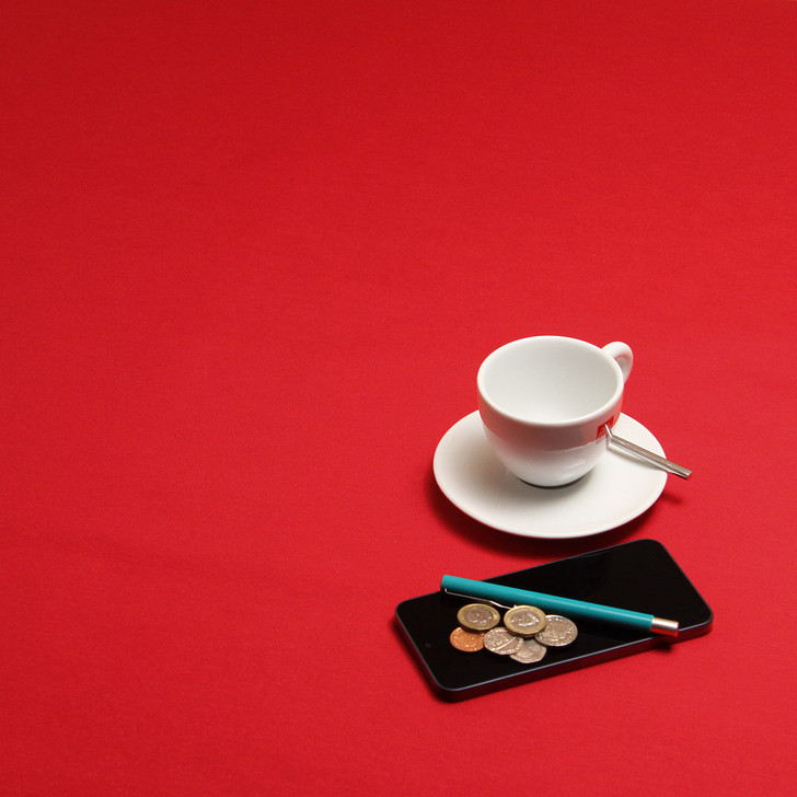 Ibiza Yarn Dyed: Festive Red -  wipe clean acrylic coated tablecloth pictured with a cup and saucer, 'phone, pen and coins.