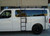 A gloss white Nissan NV van with a powder coated black side ladder, surf board mount pole, surf hooks, and roof rack from Aluminess Products.