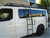 A gloss white Nissan NV van with a powder coated black side ladder, surf board mount pole, surf hooks, and roof rack from Aluminess Products.
