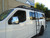 A gloss white Nissan NV van with a powder coated black side ladder, surf board mount pole, surf hooks, and roof rack from Aluminess Products.