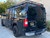 A gloss black Nissan NV van with a powder coated black side ladder, surf board mount pole, surf hooks, and roof rack from Aluminess Products.