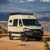 Beige Mercedes Sprinter van outfitted with several off-road accessories, parked near open canyons featuring Aluminess Explorer Roof Rack.