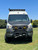 Front view of an white Mercedes Sprinter van featuring an Aluminess Explorer Roof Rack parked on the grass.