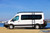 A white Ford Transit van parked in front of a bay, equipped with various off-road accessories; front winch bumper, roof rack, and side ladder.
