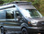 A Black Ford Transit van parked in the woods, equipped with a touring roof rack from Aluminess Products.