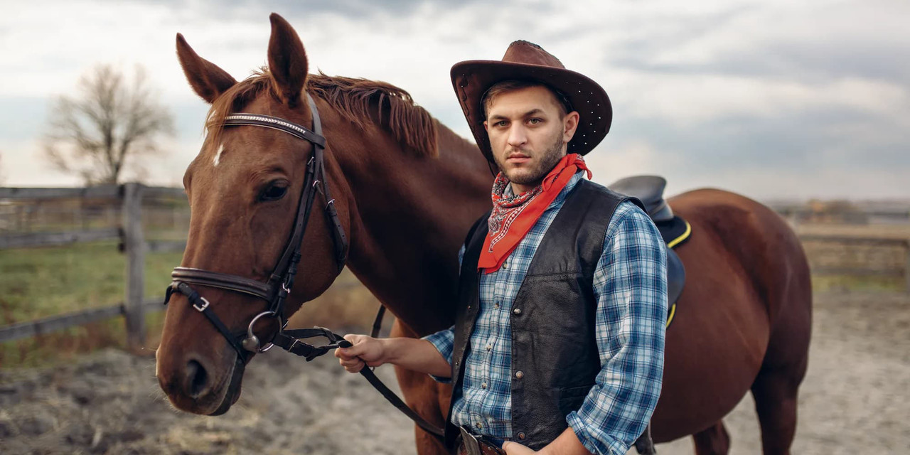 Cowboy with hat and wild rag standing next to a horse