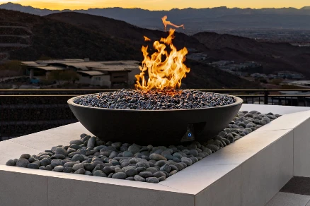 Round fire bowl with tall flames on a stone-filled patio feature overlooking mountains at sunset