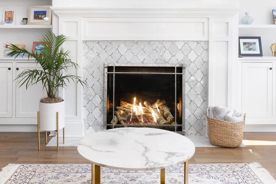 Traditional fireplace with burning logs, a patterned tile surround and white mantel in a bright living room