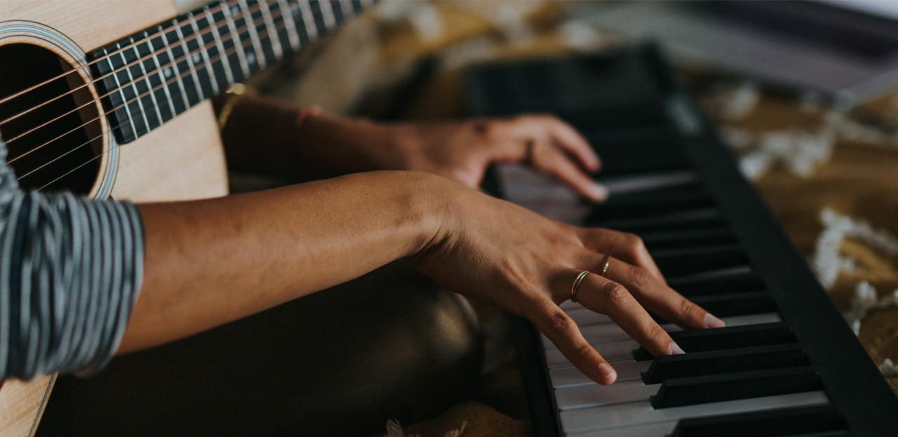 Person playing piano while holding a guitar