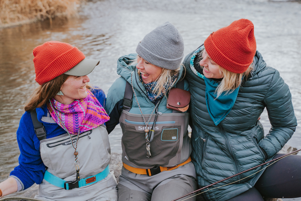 3 ladies laughing on a rock in the river wearing Damsel accessories.