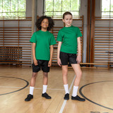 Child wearing black Velcro school plimsolls, standing on a gym floor, dressed in PE kit with a relaxed posture.