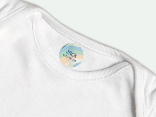 Round iron-on name label in a pastel rainbow design with a name and phone number, inside a white T-shirt