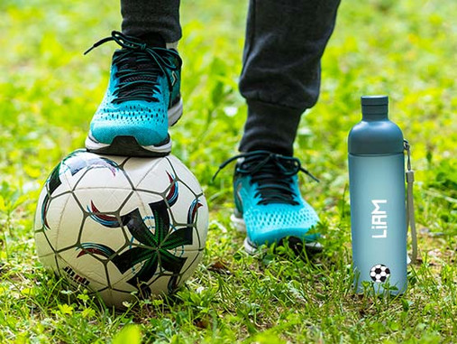 Personalised 600 ml drinking bottle named Liam with a football picture, on the grass beside a football