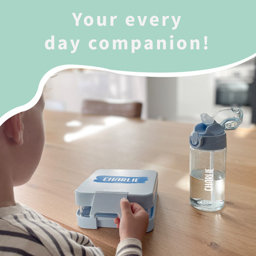 Child at a table with a light blue lunch box named Charlie and a matching water bottle
