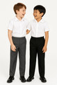 Two boys, one in grey trousers and one in black, laughing and enjoying a moment together in matching white shirts on a white background, perfect for showcasing comfort and friendship in schoolwear.