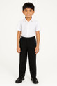 An 8-year-old Asian boy dressed in full elasticated black school trousers and a white short-sleeve shirt, smiling calmly against a clean white backdrop.