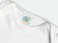 Round iron-on name label in a pastel rainbow design with a name and phone number, inside a white T-shirt
