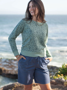 Woman walking along ocean wearing Reagan Pull-On Bermuda Short in Vintage Indigo Blue
