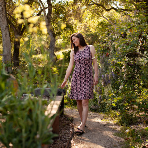 Woman walking in garden wearing Aventura Clothing Cali Fit & Flare Printed Dress with black and pink floral print.