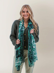 Woman holding green Winterfloral Border Scarf indoors.