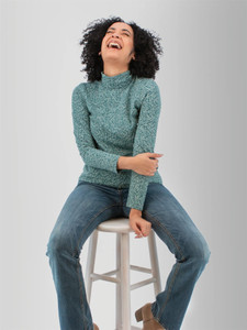 Woman sitting on stool wearing the Mariela Organic Cotton Floral Turtleneck in green.