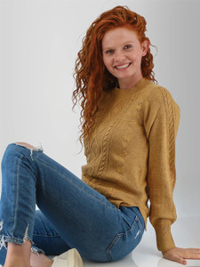 Woman sitting in studio wearing the Winter Wisteria Embroidered Cable Knit Sweater in mustard yellow.