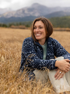 Woman sitting in field during fall wearing the Lucy Drift Reversible Microfleece Jacket in navy blue print.