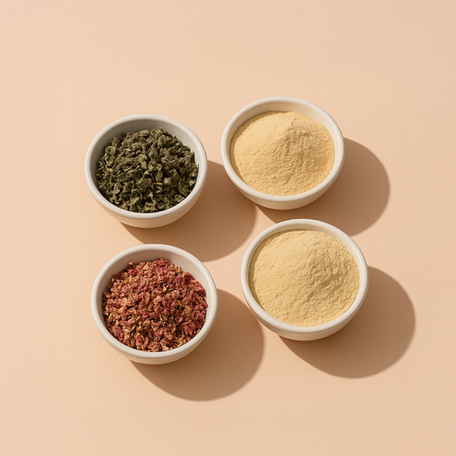 Four bowls of raspberry leaf, red clover blossom, maca root powder, and ashwagandha root powder arranged on a peach background.
