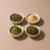 Four bowls of Relaxing Tea, ashwagandha root powder, barley grass powder, and holy basil leaf arranged on a warm pink background.