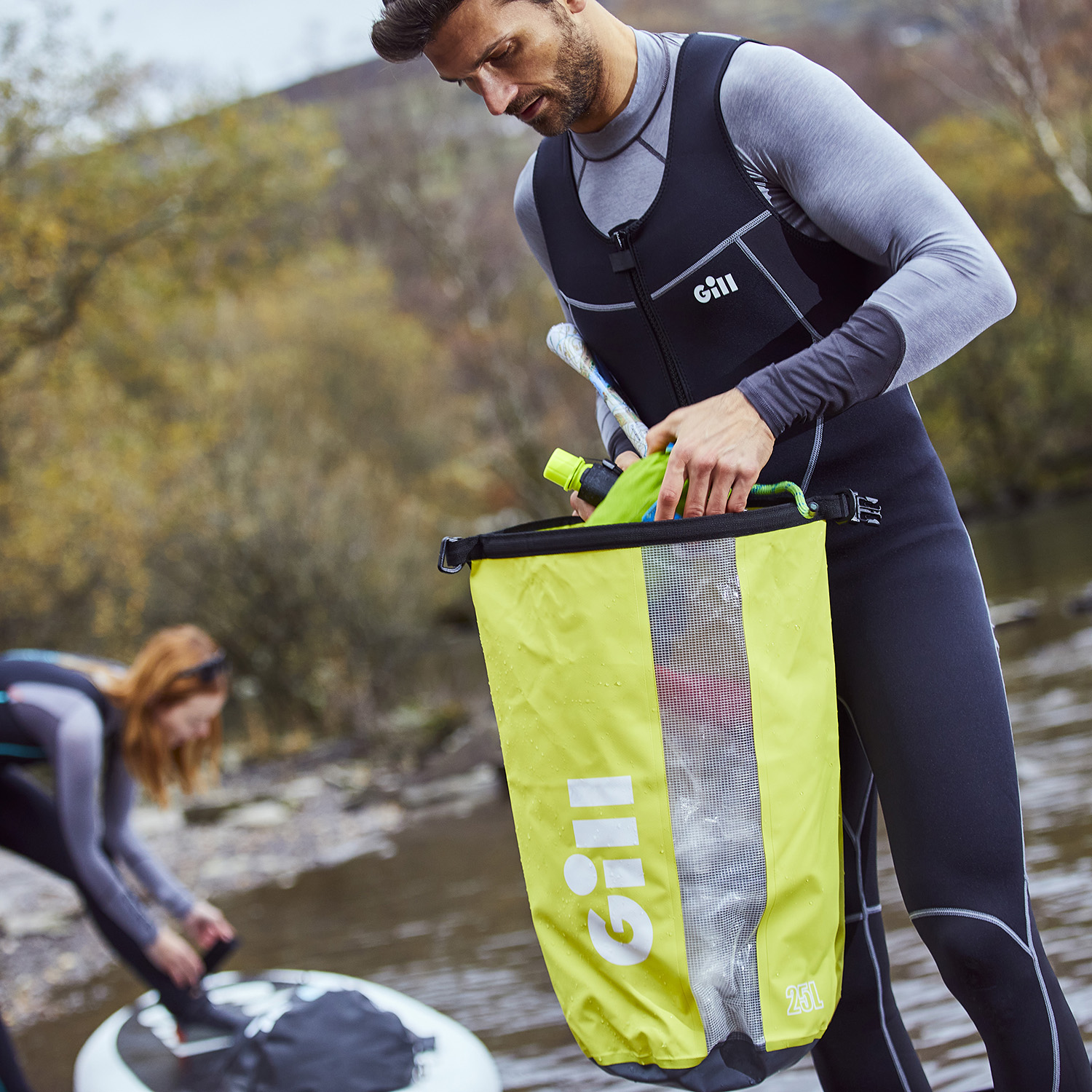 Man stood by a lake wearing a Gill Dynamic Long John and packing a Dry Cylinder Bag