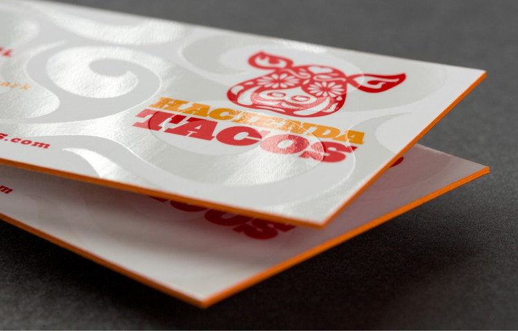 Painted edge business card with a vivid orange edge and bold red-and-orange logo print on premium cardstock — printshaQ.com