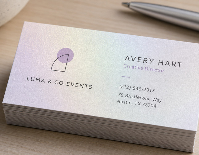 Pearl business cards photographed at an angle so the iridescent shimmer of the pearlescent stock catches the light across a minimal card design — the sheen comes from the paper itself, giving a soft satin finish without foil.